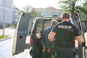 policjanci prowadzą do radiowozu zatrzymanego mężczyznę