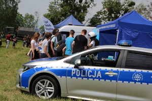 młodzież przy stoisku policyjnym , obok oznakowany radiowóz i baner promujący policję