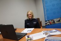 policjantka patrzy w monitor laptopa, za nią policyjny baner w kolorze niebieski, w prawym górnym rogu gwiazda policyjna