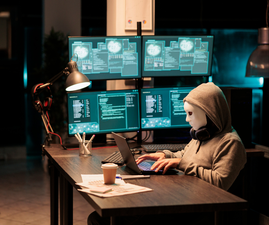 osoba w masce na twarzy, za nią 4 monitory