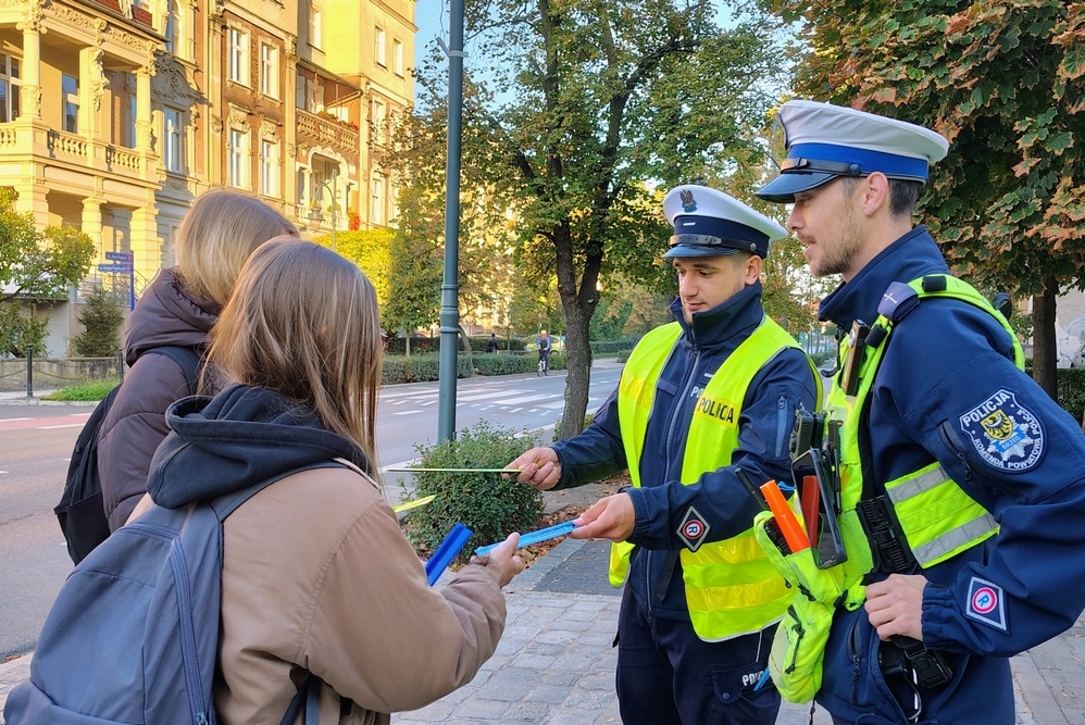 policjanci przekazują odblaski dwóm nastoletnim dziewczynom