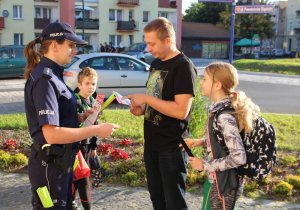 w rejonie przejścia dla pieszych umundurowana policjantka przekazuje odblaski dzieciom