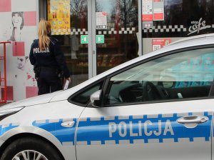 policjantka wchodzi na stację paliw. Przed budynkiem zaparkowany radiowóz