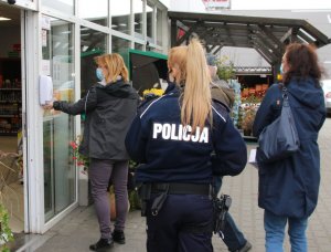 policjantka, osoby postronne i pracownice stacji sanitarnej przed budynkiem stacji paliw