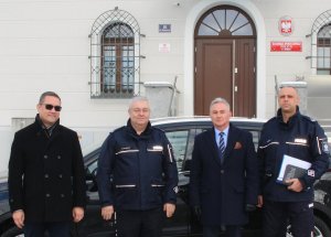 4 mężczyzn na tle ciemnego pojazdu i budynku