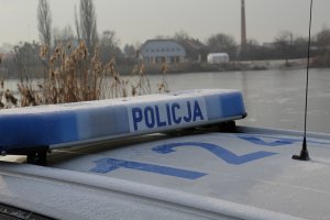 belka z napisem POLICJA na radiowozie, w tle zamarznięty zbiornik wodny