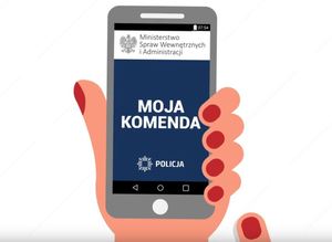 w dłoni telefon komórkowy, z grafiką aplikacji Moja Komenda