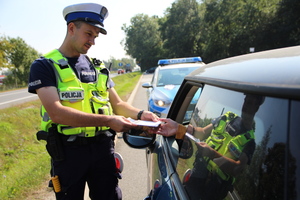 umundurowany policjant przekazuje materiały edukacyjne kierowcy