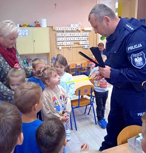 policjant rozdaje dzieciom książeczki