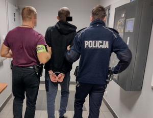 policjanci prowadzą zatrzymanego mężczyznę w kajdankach zapiętych na ręce trzymane z tyłu