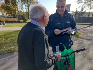 umundurowany policjant przekazuje materiały edukacyjne seniorowi który prowadzi rower