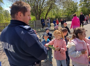 umundurowany policjant rozdaje dzieciom książeczki