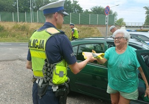 policjant przekazuje kobiecie kamizelkę odblaskową