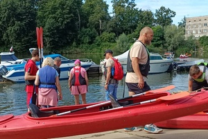 grupa osób nad wodą i kajaki