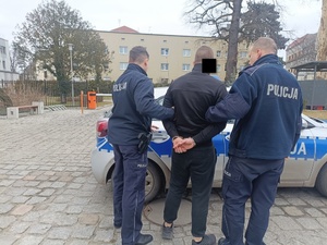 policjanci prowadzą zatrzymanego mężczyznę do radiowozu