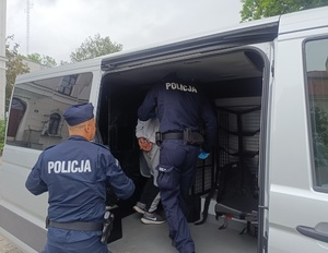 umundurowani policjanci prowadzą zatrzymanego do radiowozu