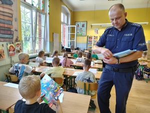 policjant rozdaje książeczki dzieciom