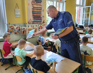 policjant rozdaje książeczki dzieciom
