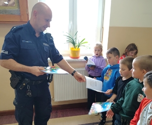 policjant przekazuje książeczki dzieciom