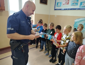 policjant przekazuje książeczki dzieciom