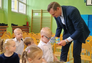 Mężczyzna w garniturze przekazuje dzieciom książeczki odblaskowe