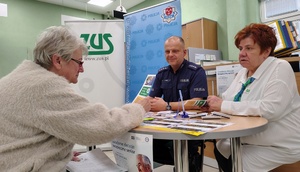 trzy osoby siedzą przy biurku z ulotkami