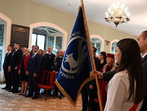 grupa osób, przed nimi sztandar uczelni