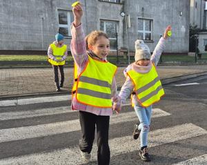 dzieci w odblaskowych kamizelkach przechodzą przez pasy