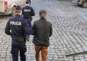 Umundurowany policjant prowadzi zatrzymanego mężczyznę