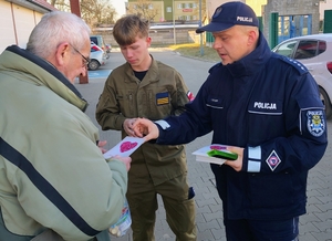 policjanci wraz z młodzieżą rozdają ulotki i odblaski seniorom