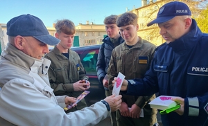 policjanci wraz z młodzieżą rozdają ulotki i odblaski seniorom