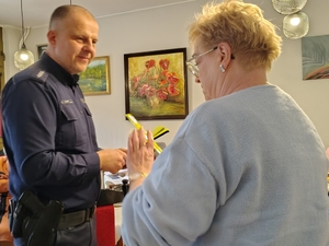 policjant przekazuje elementy odblaskowe seniorom