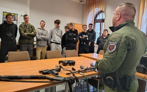 policjant w mundurze instruktora strzelectwa  pokazuje broń młodzieży