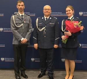 troje policjantów, za nimi granatowy banek z napisami Ministerstwo Spraw Wewnętrznych i Administracji